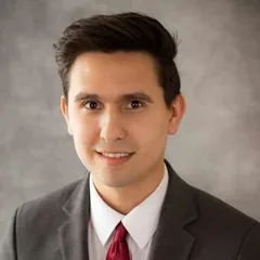 Andrew Valentin, associate attorney at Schuster Law, smiling in a grey suit and dark red tie