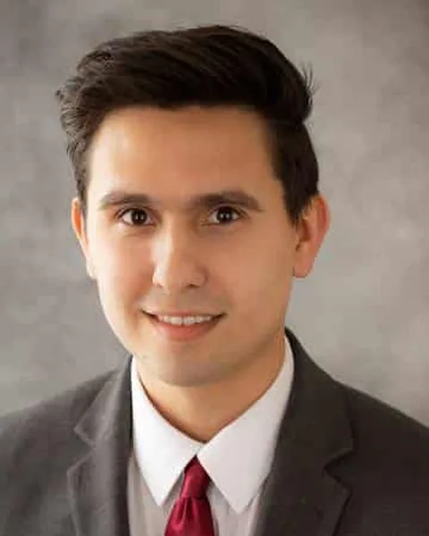 Andrew Valentin, associate attorney at Schuster Law, smiling in a grey suit and dark red tie