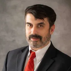 Christopher D. Gasda, associate attorney at Schuster Law, bearded and wearing a dark suit with a red tie