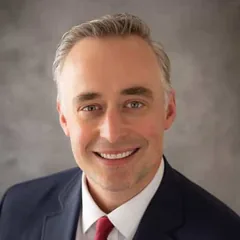 Justin M. Bernstein, associate attorney at Schuster Law, smiling in a navy suit and red tie