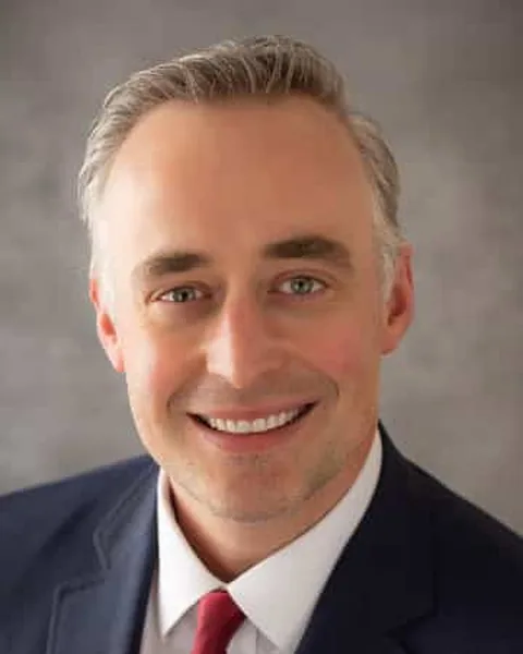 Justin M. Bernstein, associate attorney at Schuster Law, smiling in a navy suit and red tie